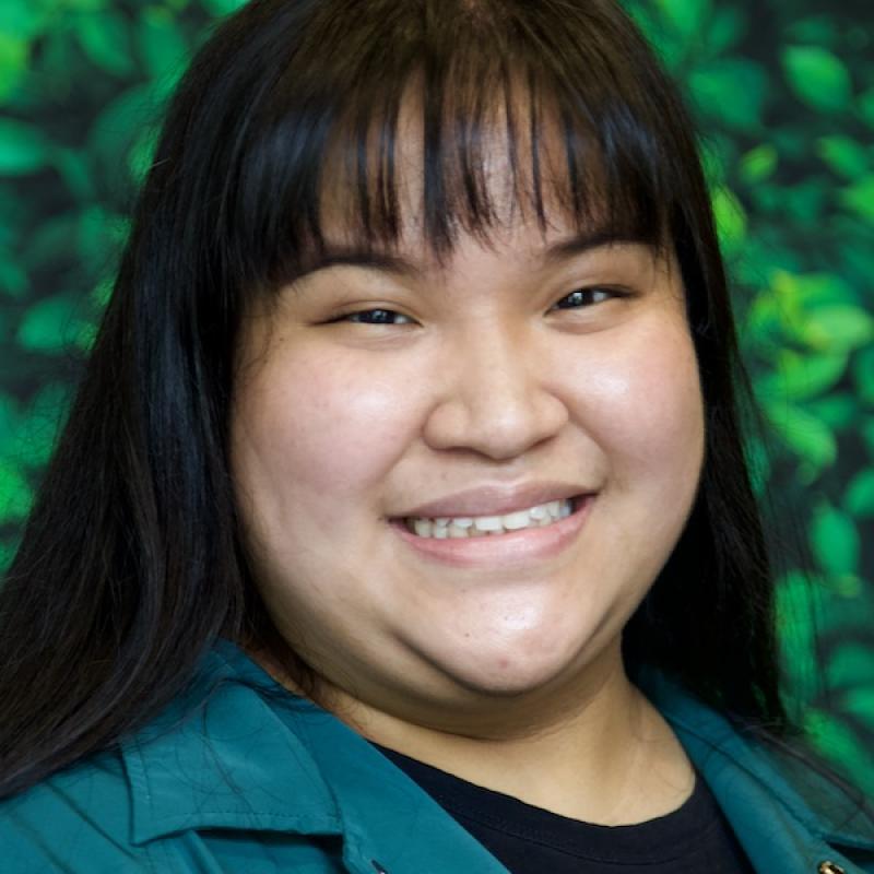 A photo of Christine Samala wearing a green cardigan and black shirt with a green background.