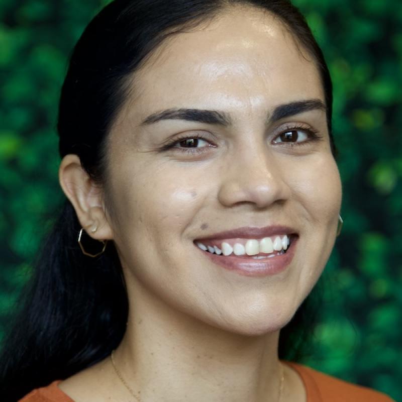 A photo of Mariela Cruz-Aguilera wearing a sandstone shirt with a green background.