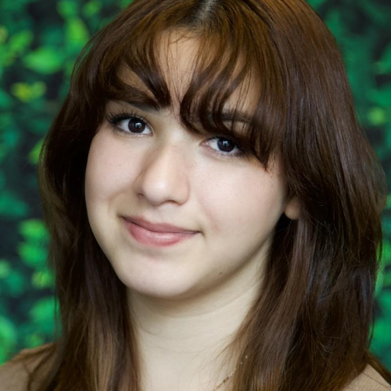 A photo of Vianney Caravantes wearing a brown shirt with a green background.